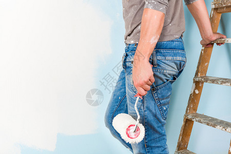 画家穿着喷溅的衬衫用油漆滚筒刷墙图片