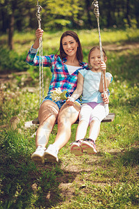 年轻的母亲带着女儿在春天的花园里荡秋千图片