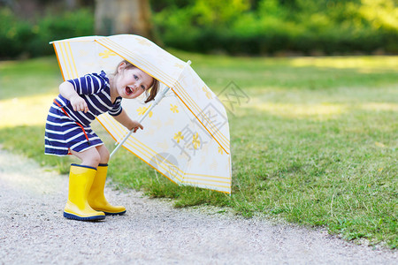 可爱的小孩女玩得开心穿着黄雨靴带雨伞在图片