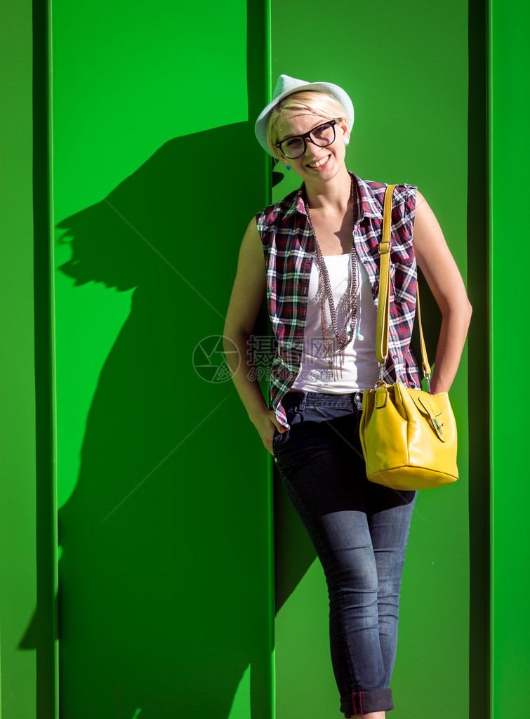 黄色袋子靠在绿墙上的时髦女孩的画像图片