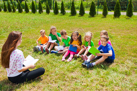 年轻的老师和孩子们坐在草地上看书图片