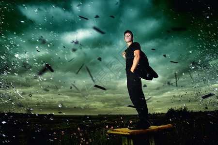 在暴风雨中站在田野中间的英俊年轻男子深绿天空背背景图片