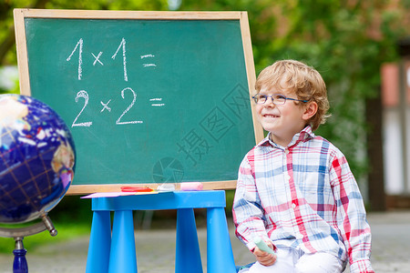 有趣的小孩戴着眼镜在黑板上练习数学图片