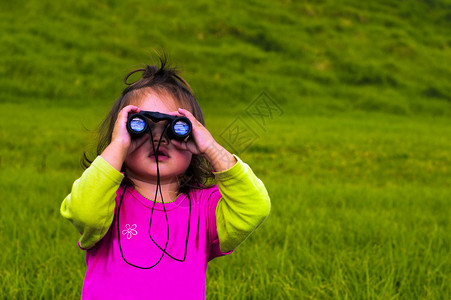 小女孩通过双筒望远镜看背景图片