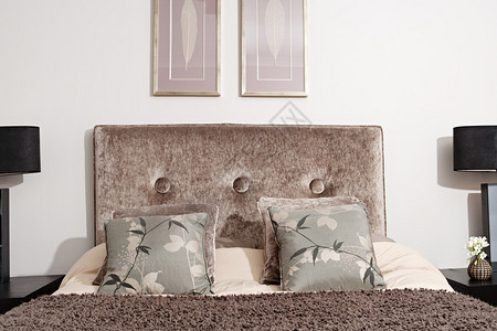 室内设计师在优雅的旅馆卧室内用灯具和侧桌垫子和枕头观看天鹅绒床头图片