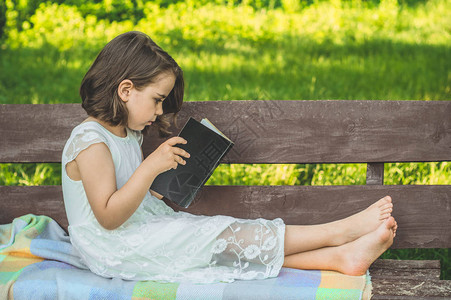 小女孩手里拿着书在户外看书坐在长椅上看书的女孩图片