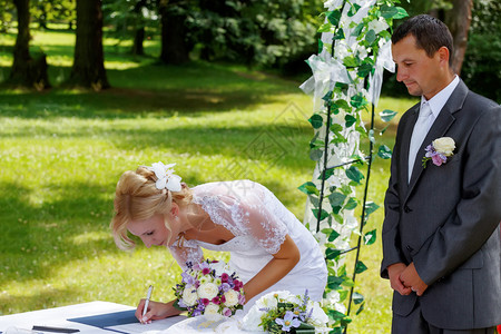 美丽的金碧美丽微笑的新娘在户外绿草地上签了婚约图片