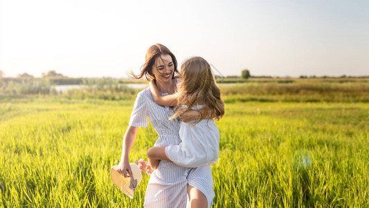 美丽幸福的母女在日落时分拥抱在绿色的田野中图片
