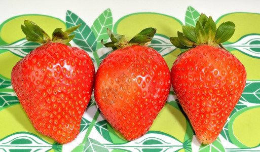 五颜六色的绿色背景上的三个草莓背景图片