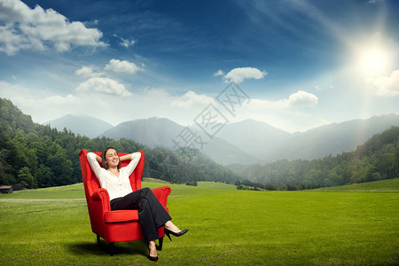 坐在绿草地上的红椅子上与山丘森林和天空相伴的图片