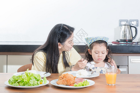 亚裔女孩对母亲喂饭时吃大米表示厌恶而背景图片