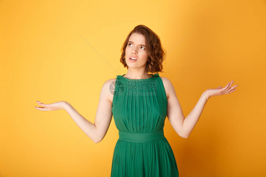 用橙色隔离的双臂张开的困惑女人的肖像图片