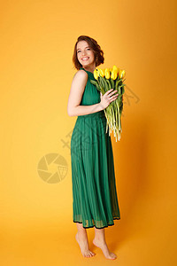 身着绿装的笑脸女人带着黄色的郁金香花束在图片