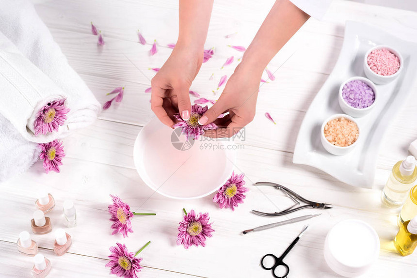 女在餐桌上用鲜花毛巾五颜六色的海盐芳香油瓶指甲油奶油容器和美容沙龙修指甲工具在浴缸里扔花图片