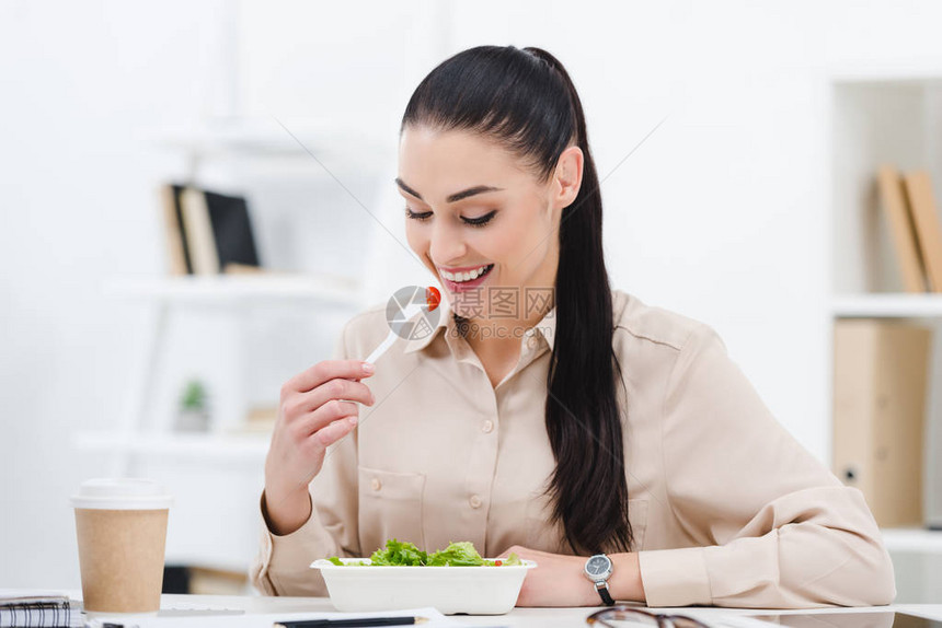笑着吃东西的女商人在办公室午餐图片