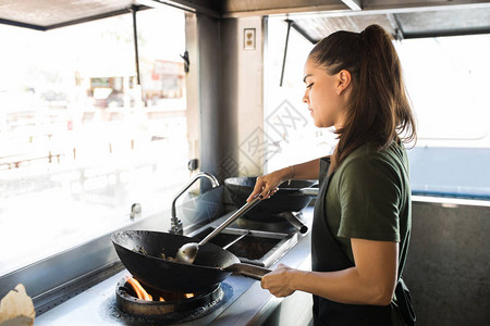 漂亮的年轻女厨师在她的餐车里用炒锅烹制图片