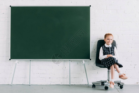 可爱的小女学生坐在黑板上坐椅时在图片