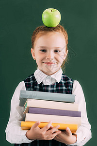 可爱的红发小女学生头上有苹果拿着一堆书图片