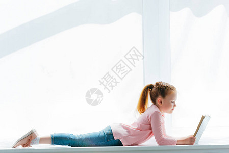 可爱的小女生躺在窗台上看书的侧视图图片
