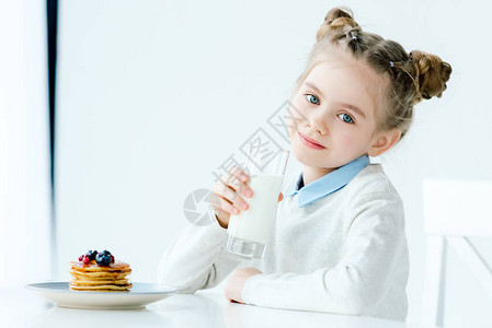 微笑的孩子的肖像手拿着牛奶和自制煎饼桌上图片