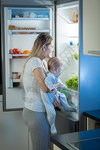 母亲和婴儿子的肖像晚上在冰箱里找东西吃图片
