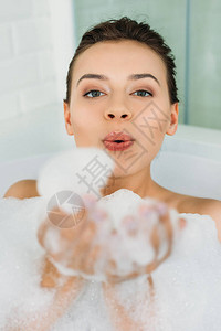 美丽的年轻女士在浴室里吹发泡背景图片