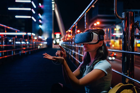 坐在街上与夜市背景相伴的虚拟现实头盔图片