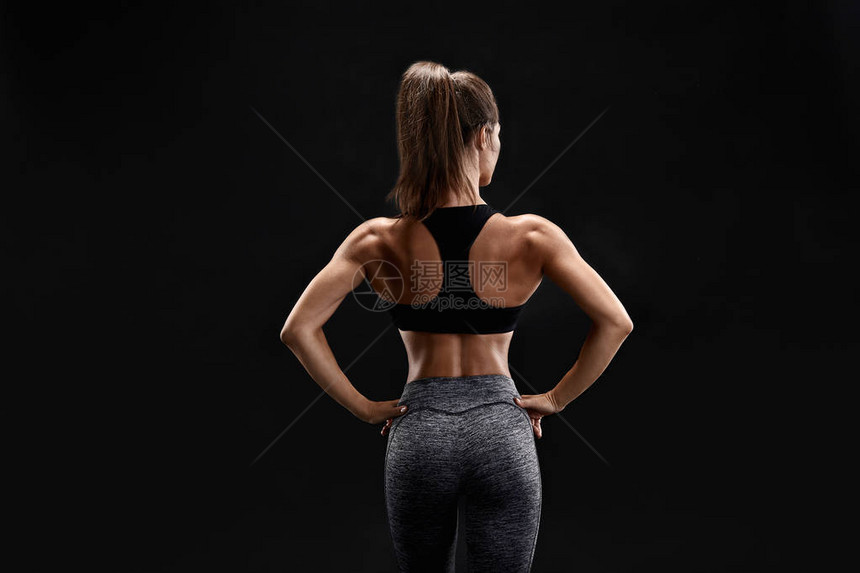 一个穿着服腹部肌肉发达的女强人的镜头摆在黑色背景上的健身女模特一个女人背着她站图片