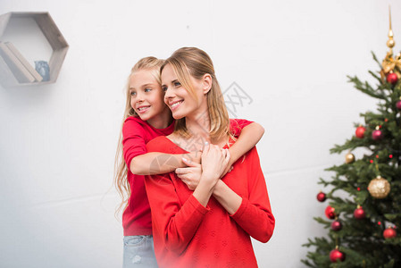 快乐的母亲和女儿在圣诞节树上拥抱着欢乐图片