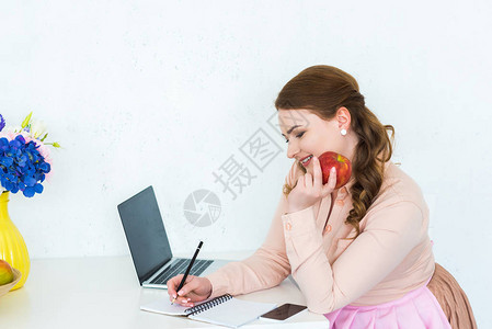 美丽的女人写点笔记本在厨房拿着苹果图片