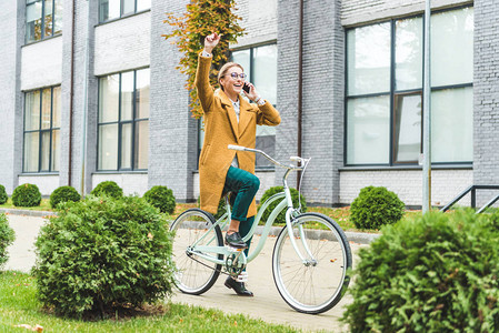 开心的女子在公园骑自行车时挥舞和用图片