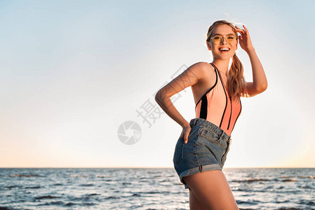 穿着太阳镜泳衣和牛仔短裤的美丽的年轻女士图片