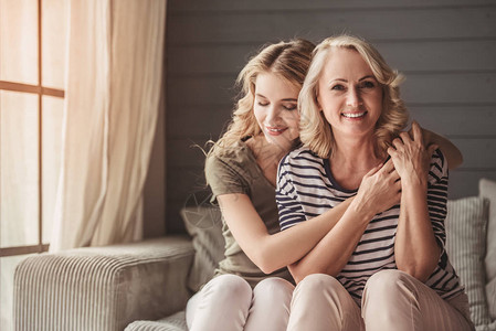 美丽的老妈和成年女儿在家中坐在沙发上时拥图片