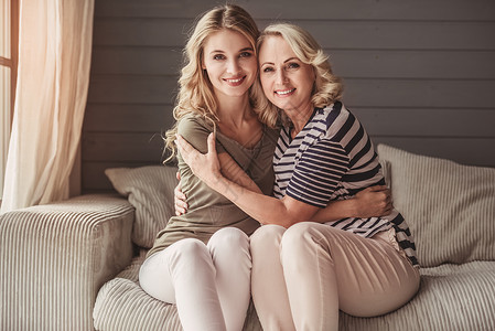 漂亮的老妈和她成年的女儿坐在家里的沙发上拥抱看图片