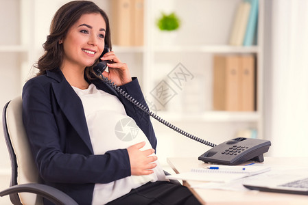 快乐的孕妇在办公室工作时通电话图片