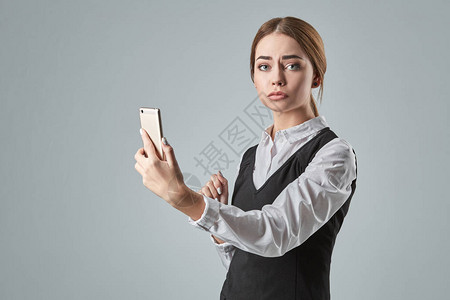 使用室内灰色背景移动电话的漂亮年轻商业女青年图片