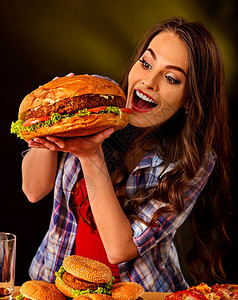 女人吃汉堡学生吃快餐非常大的汉堡的女孩咬女孩想吃很多垃圾在黑色背景上宣传快餐大忙背景图片