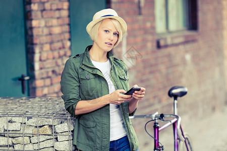 时髦年轻漂亮的女孩在城市城市场景中使用智能手机和老式公路自行车图片