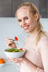 美丽的年轻金发美女吃新鲜健康蔬菜沙拉背景图片