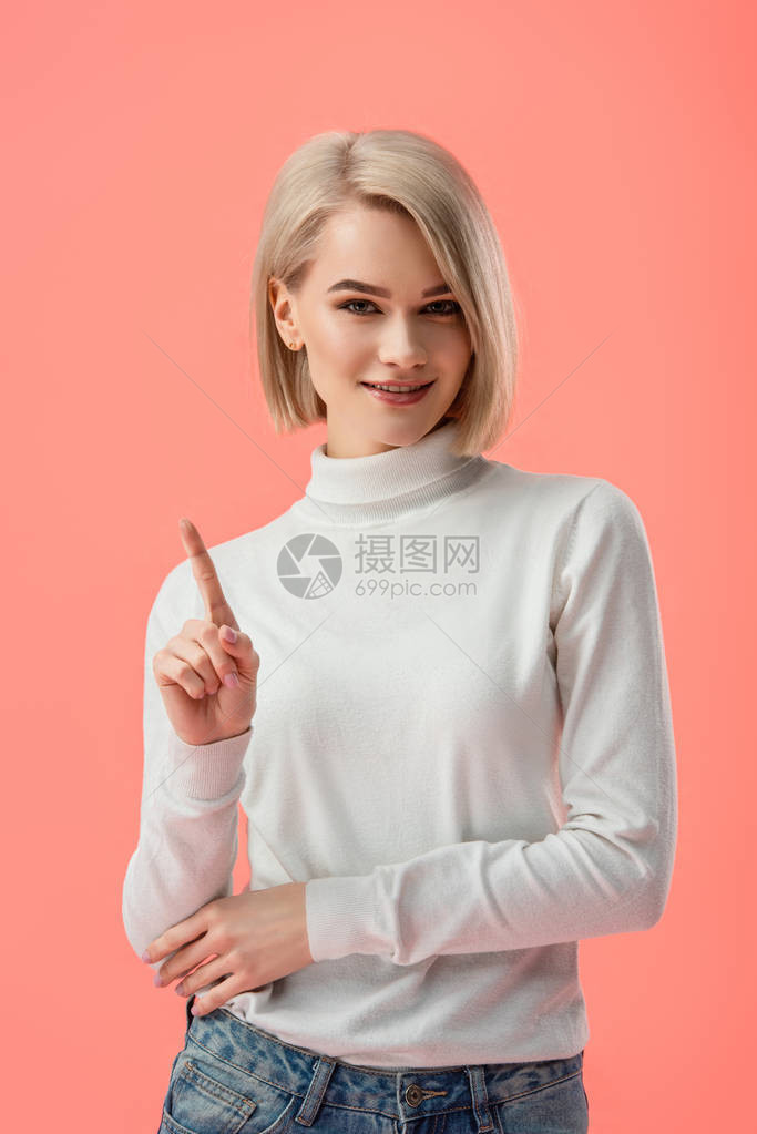 漂亮的金发女孩站着用手指着在粉红色上图片