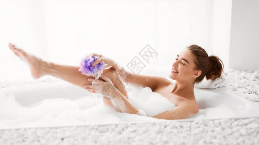 在浴缸里用泡沫洗海绵的妇女图片