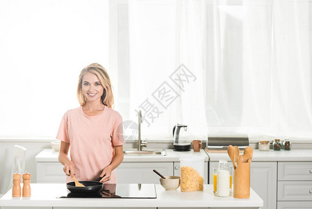 美丽的女人早上在厨房用煎锅和铲子做饭图片