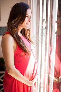 一位年轻孕妇在阳光明媚的日子站在窗前的窗口图片