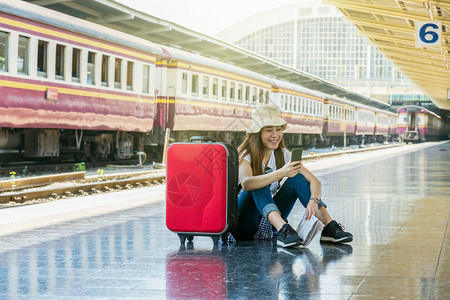 亚洲女旅行者在去火车站旅行前坐着看智能手机旅行和图片
