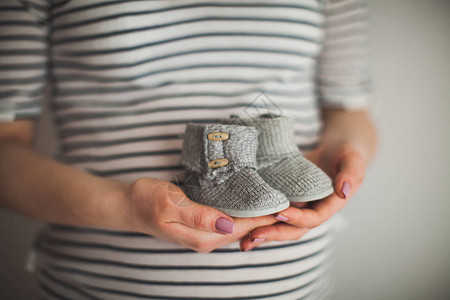 一只手拿着一双小鞋子这是灰色背景的婴儿鞋母婴主题怀孕图片