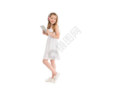 带着平板电脑的耳机中快乐的小女孩看着在白色上图片