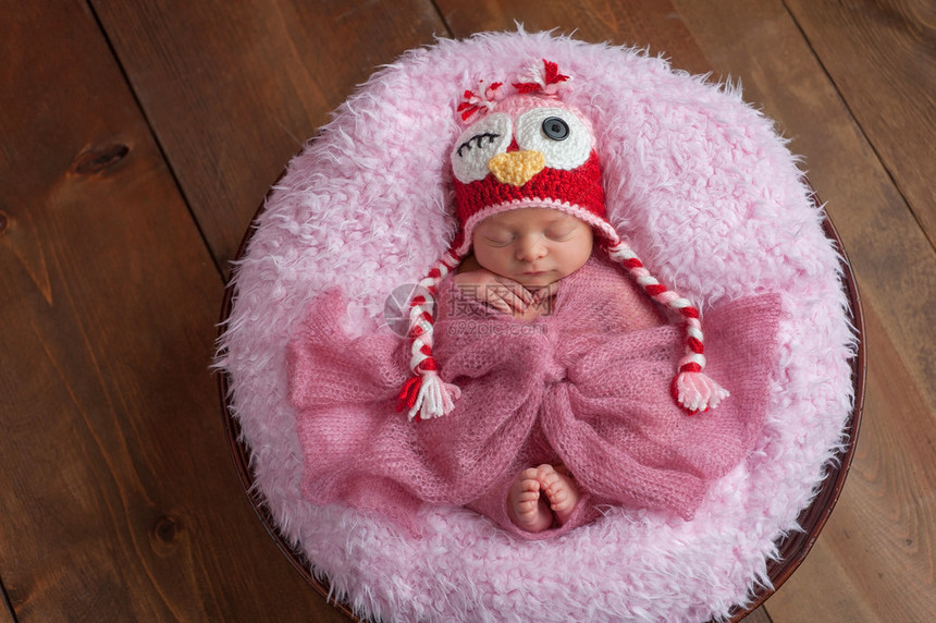 一个六天大的新生女婴睡在一个木碗里她戴着一顶粉和的钩编感猫头鹰帽子在木背景图片