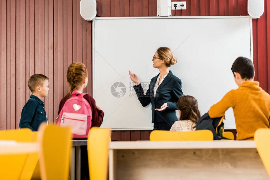 背着书包的学童看着老师在交互式白板上图片
