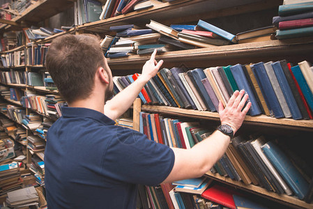 男人从旧图书馆的书架上挑选一本书一个学生在图书馆找书文学的选择书架上放着书背景图片
