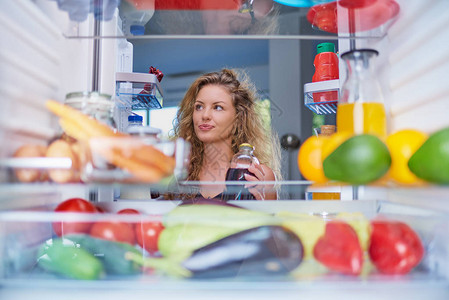 女人站在装满杂货的冰箱前寻找吃的东西从冰箱内图片